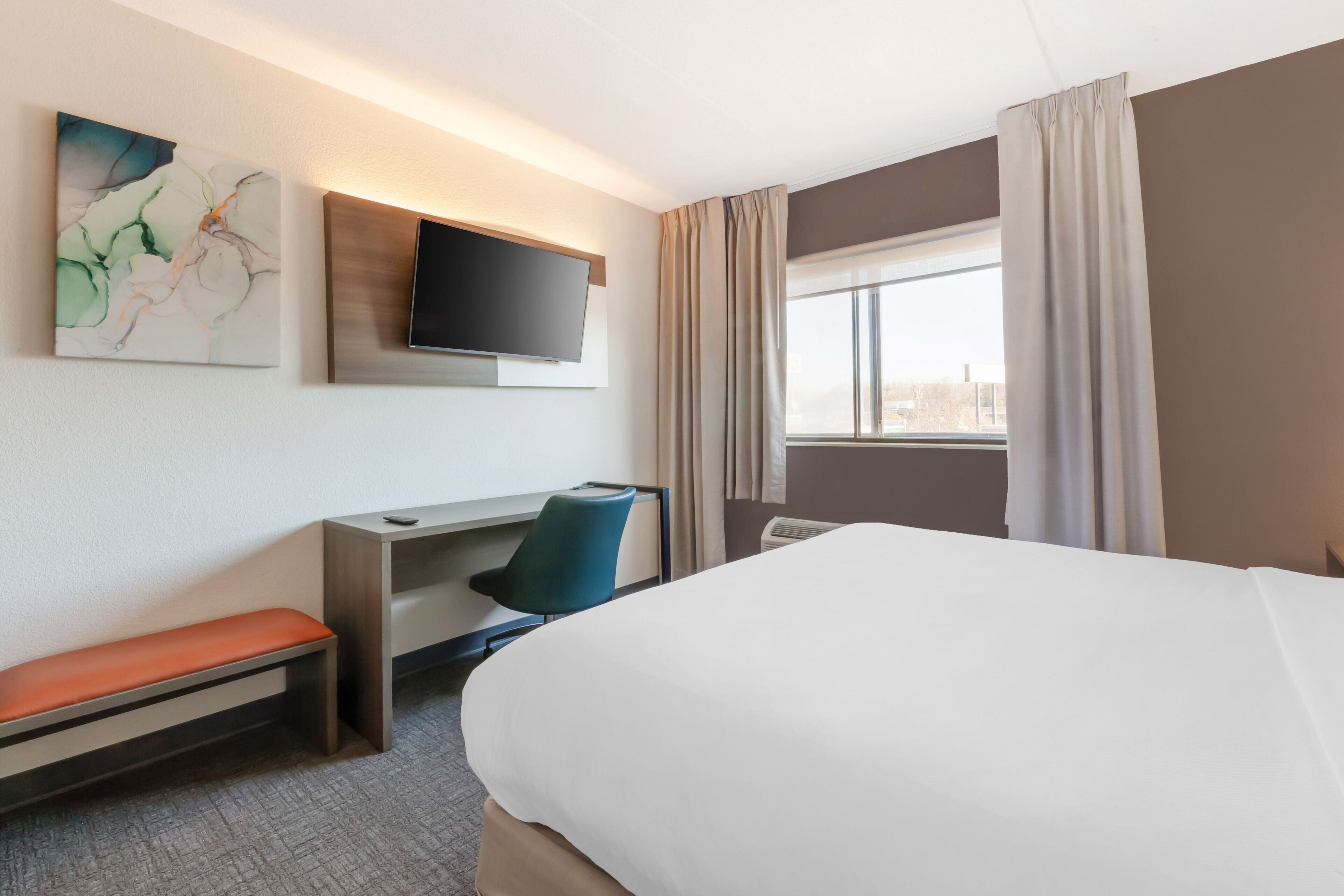 A hotel room with a bed, a desk, a chair, a television, and a window with curtains.