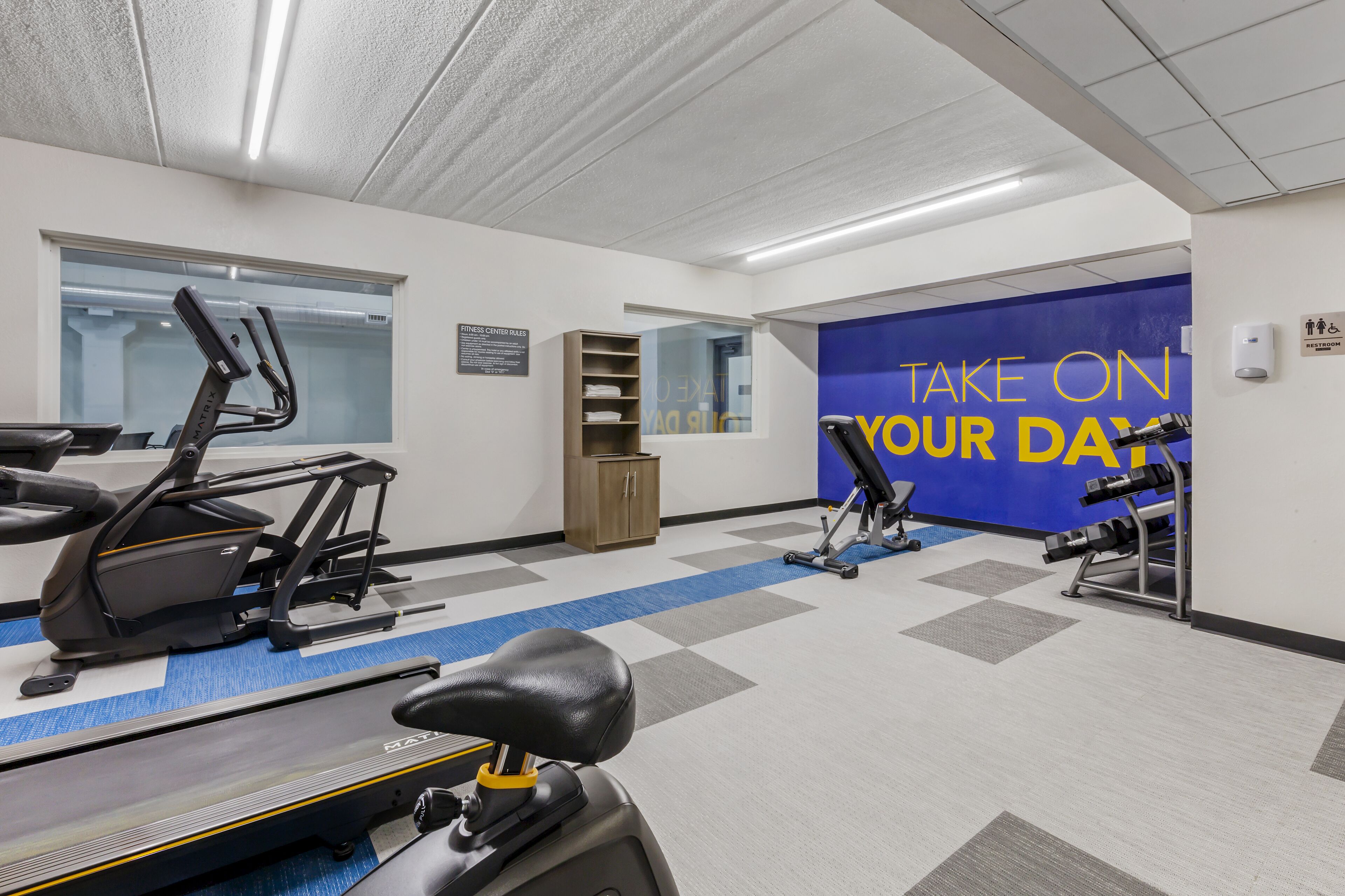A gym with exercise equipment, a blue wall with motivational text, and a window.