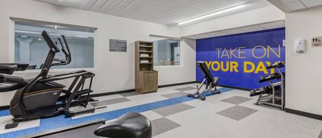 A gym with exercise equipment, a blue wall with motivational text, and a window.
