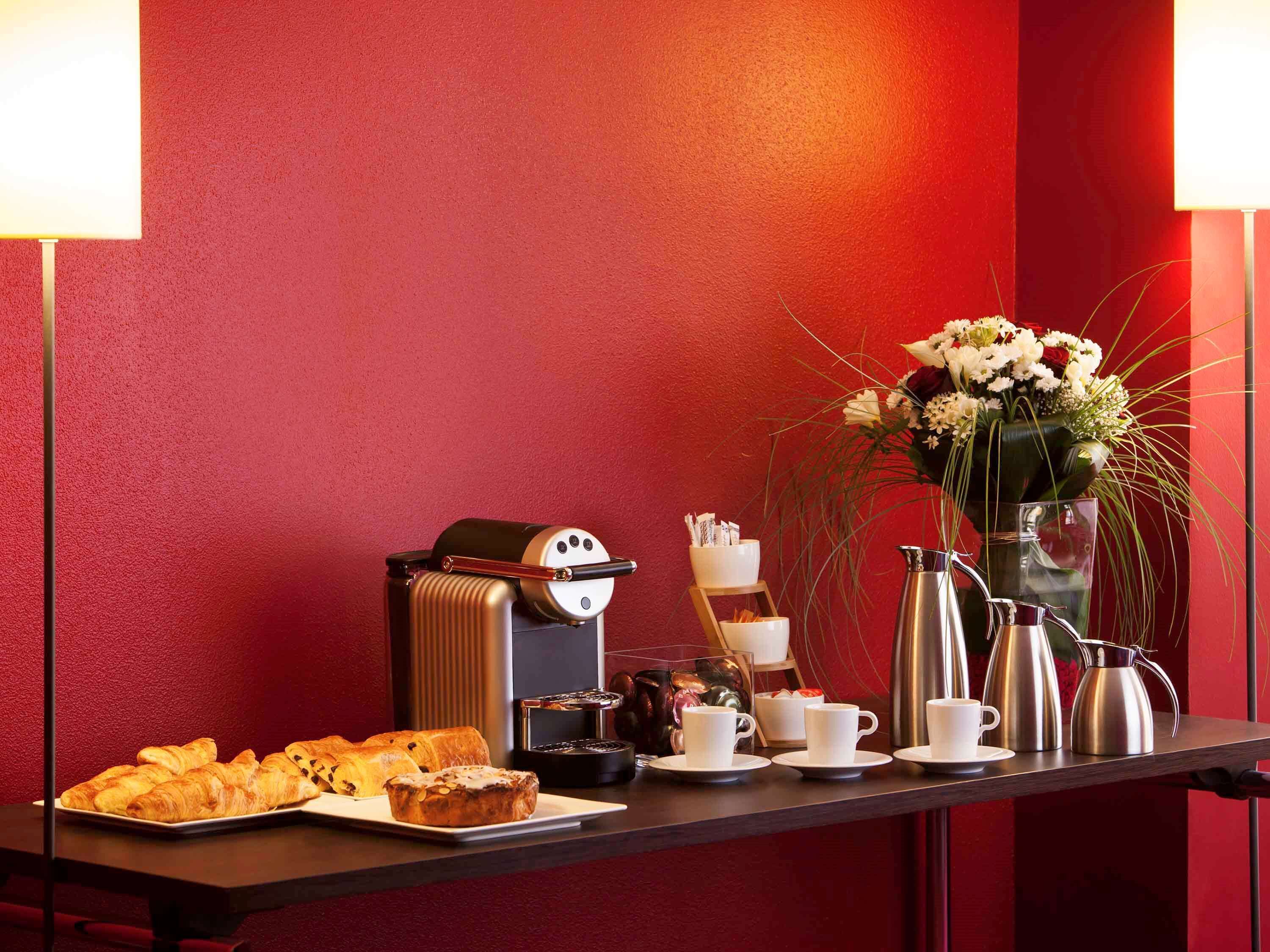 Een ontbijtbuffet met gebak, koffie en thee op een tafel tegen een rode muur.