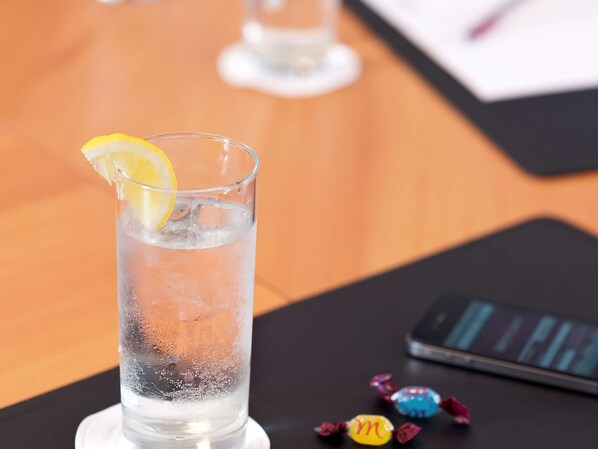 A glass of water with a lemon slice on a coaster, a smartphone, and some wrapped candies on a table. - Hôtel Mercure Strasbourg Centre (Strasbourg)