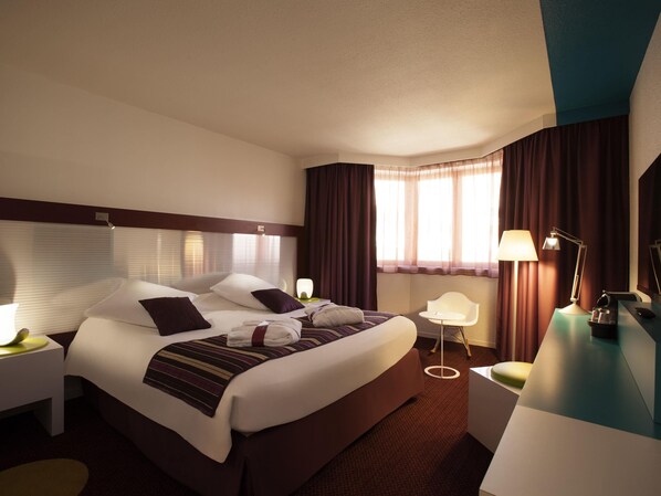 Ein Hotelzimmer mit einem großen Bett, Nachttischen, einem Schreibtisch, einem Stuhl und einem Fenster mit Vorhängen.