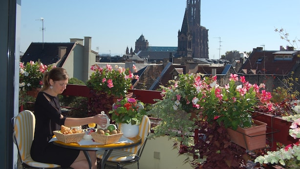 A balcony with a table set for a meal, surrounded by potted plants and flowers. - Hôtel Mercure Strasbourg Centre (Strasbourg)