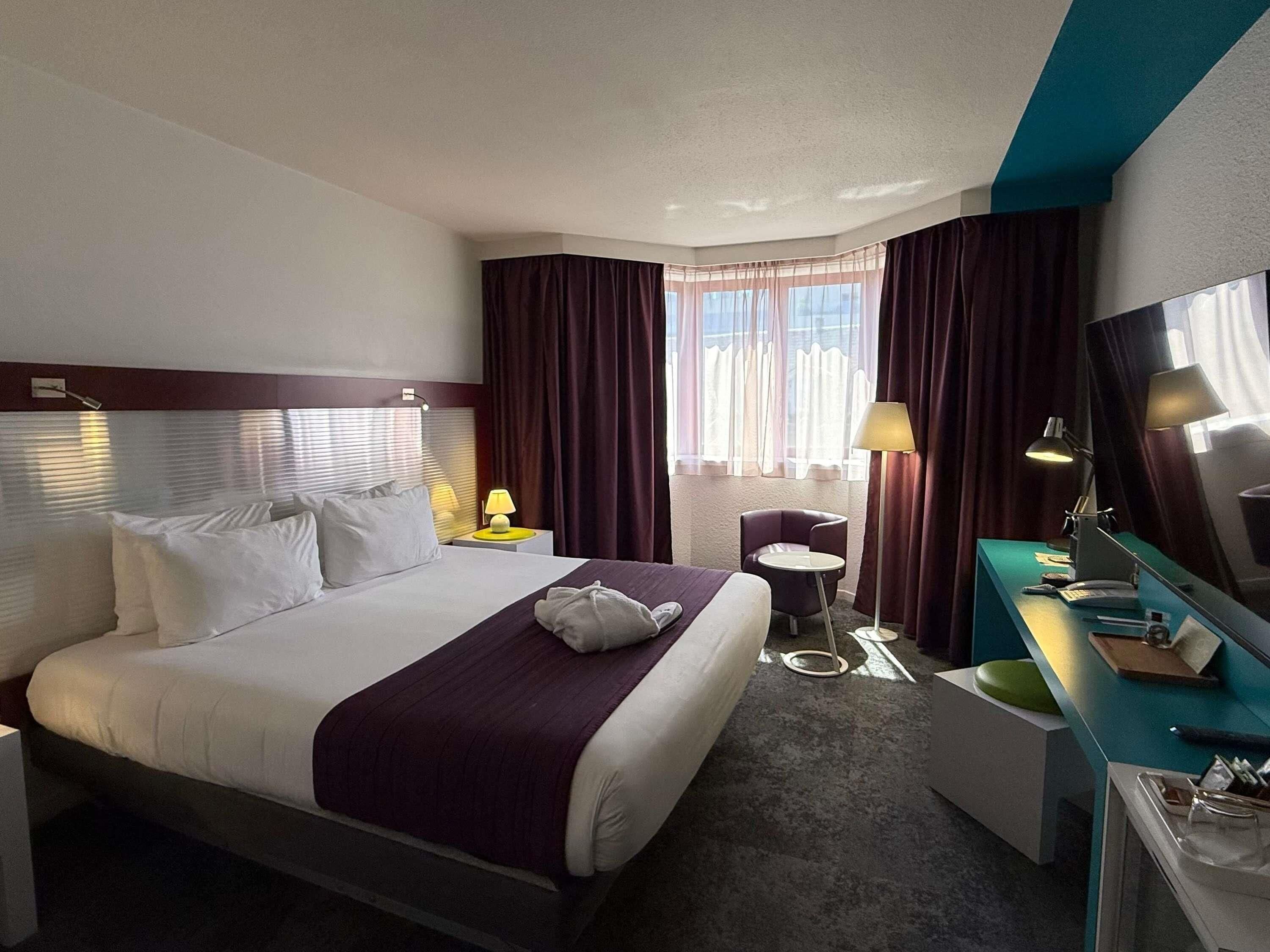 Une chambre d’hôtel comprenant un lit, une table de chevet, une lampe, une chaise, un bureau et un grand miroir.