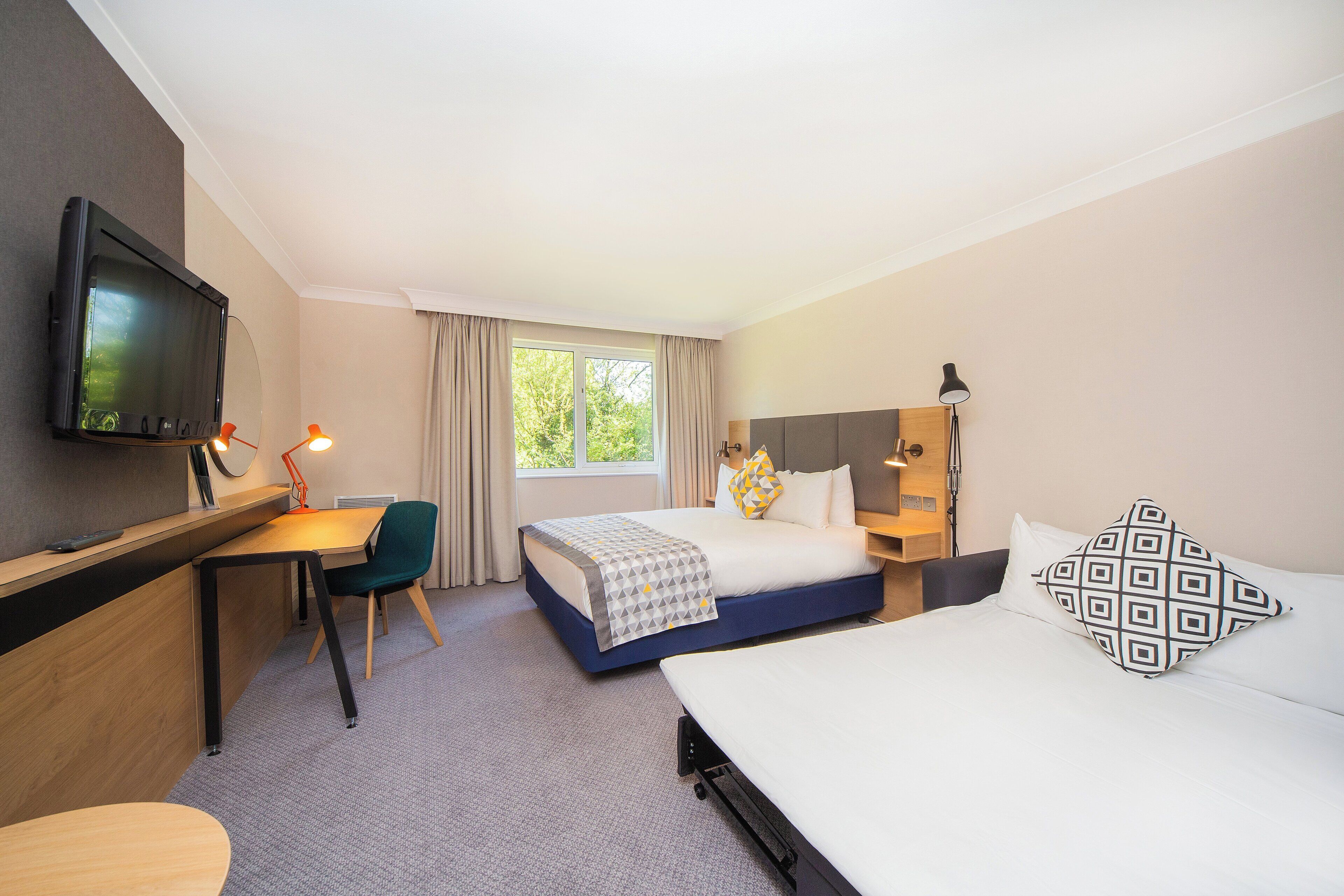 A hotel room with a bed, a desk, a chair, a TV, and a window.
