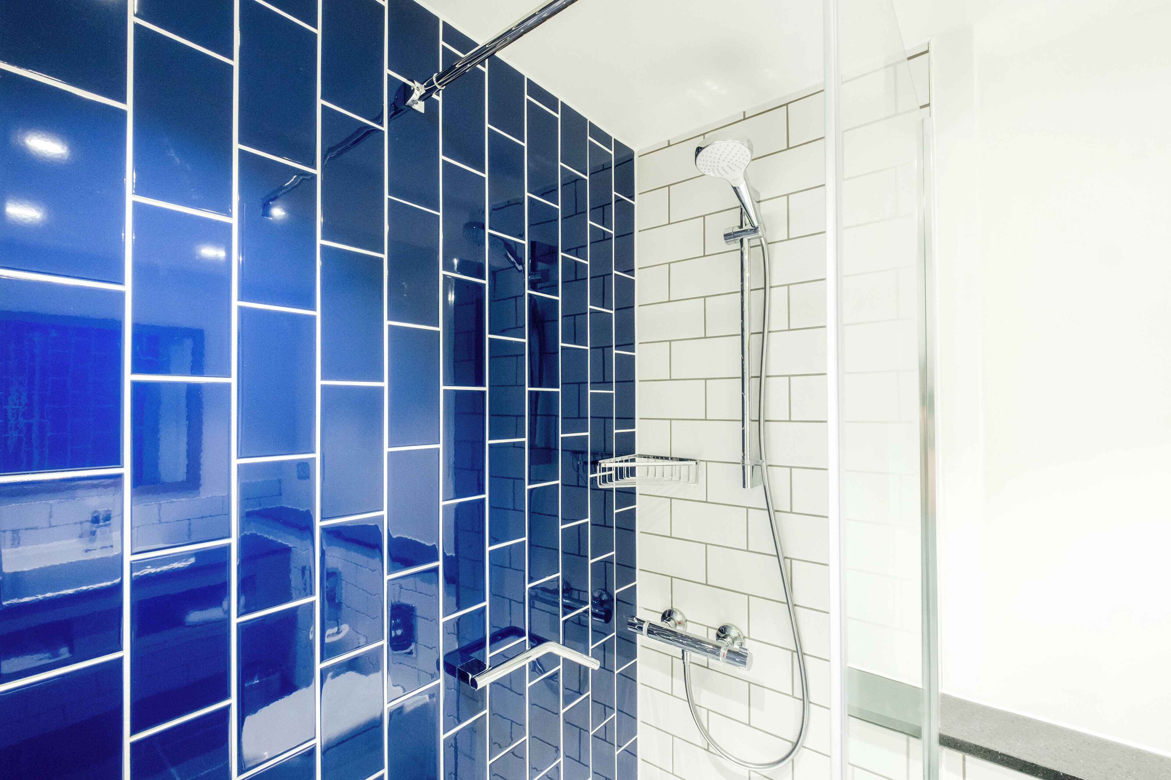 Ein Badezimmer mit blau gefliesten Wänden, einer Dusche inklusive Handbrause und einer Duschkabine aus Glas.