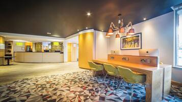 Un vestíbulo de hotel con mostrador de recepción, zona de estar y alfombra estampada.