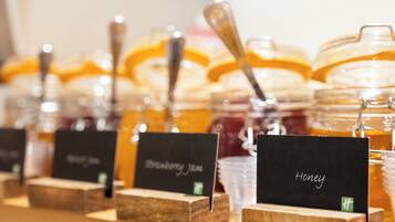 Potten honing en aardbeienjam met houten standaardjes en zwarte etiketten.
