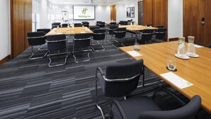 A conference room with a large table, multiple chairs, and a presentation screen displaying the Holiday Inn logo. - Holiday Inn Reading South M4 Jct11 by IHG (Reading)