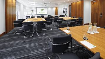 Un salón de conferencias con una gran mesa, varias sillas y una pantalla mostrando el logotipo de Holiday Inn.