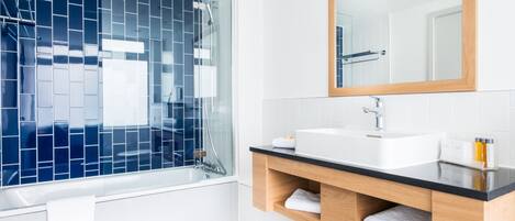 A modern bathroom with a glass-enclosed shower, white tiles, a wooden vanity, and a large mirror.