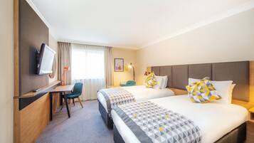 Quarto de hotel com duas camas, uma mesa, uma cadeira, uma televisão e uma janela com cortinas.