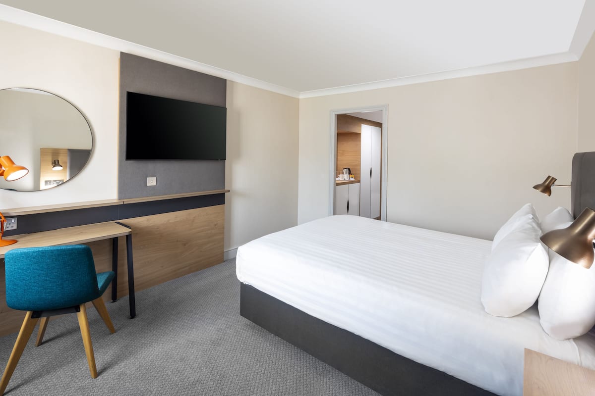 A hotel room with a bed, a desk, a chair, a TV, and a mirror.