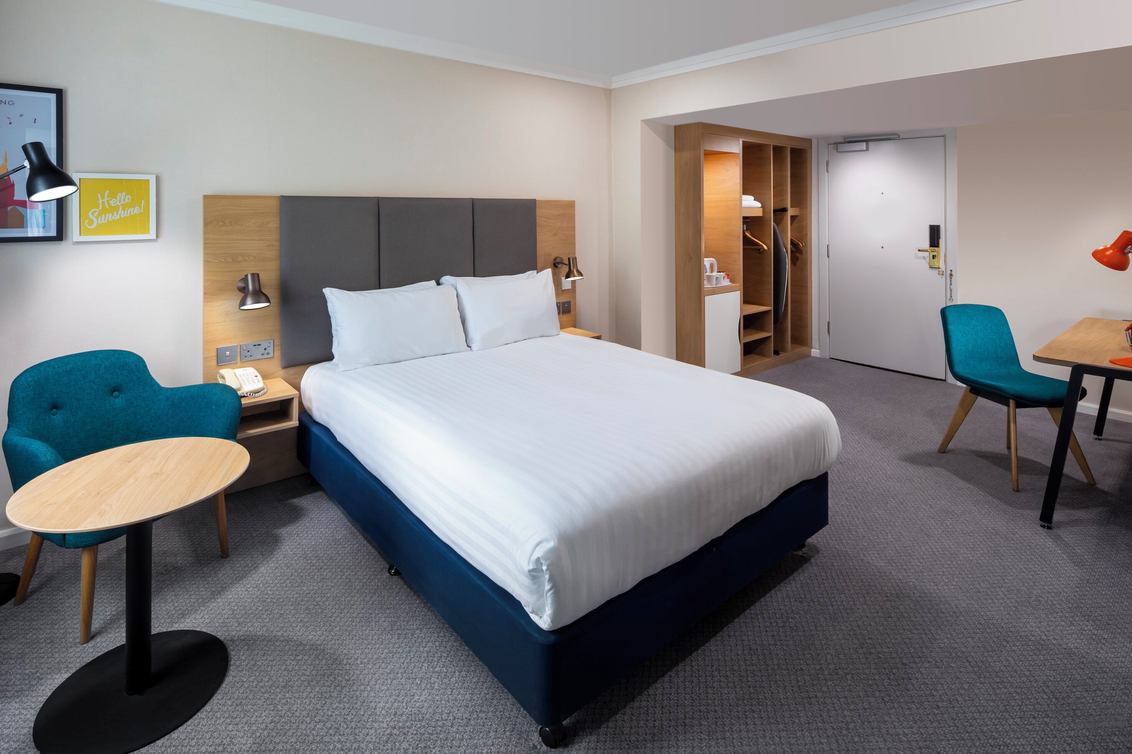 Una habitación de hotel con una cama grande, un escritorio con silla, un armario y una pequeña mesa con otra silla.