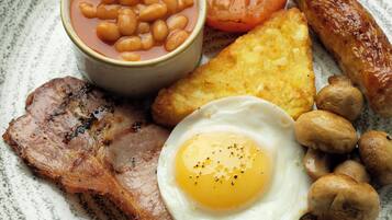Un plato de desayuno con tocino, huevos, salchichas, champiñones, tostadas, frijoles y tomate.