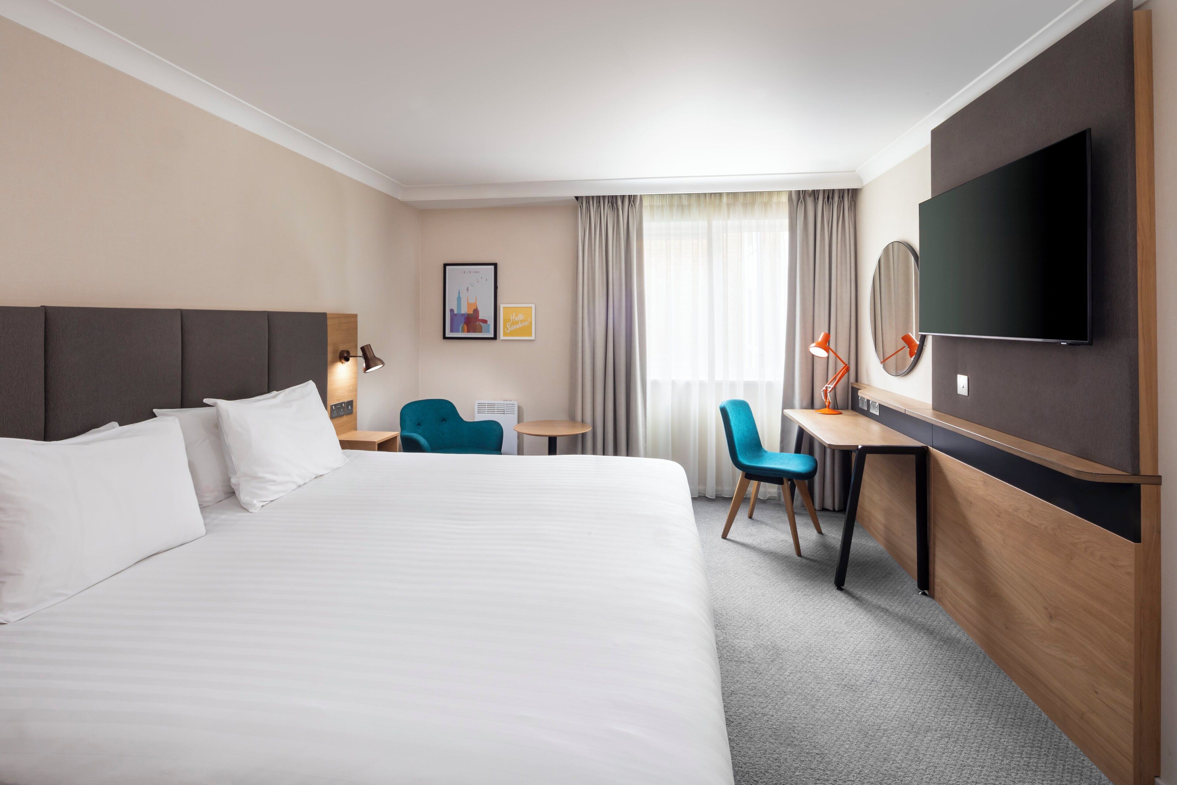 Una habitación de hotel con una cama grande, un escritorio, una silla, un televisor y una ventana con cortinas.