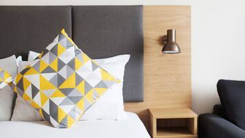 Una cama con un cojín estampado con motivos geométricos, una mesita de noche, una lámpara y una silla.