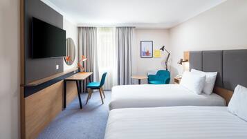 A hotel room with two beds, a desk, a chair, a TV, and a window with curtains.