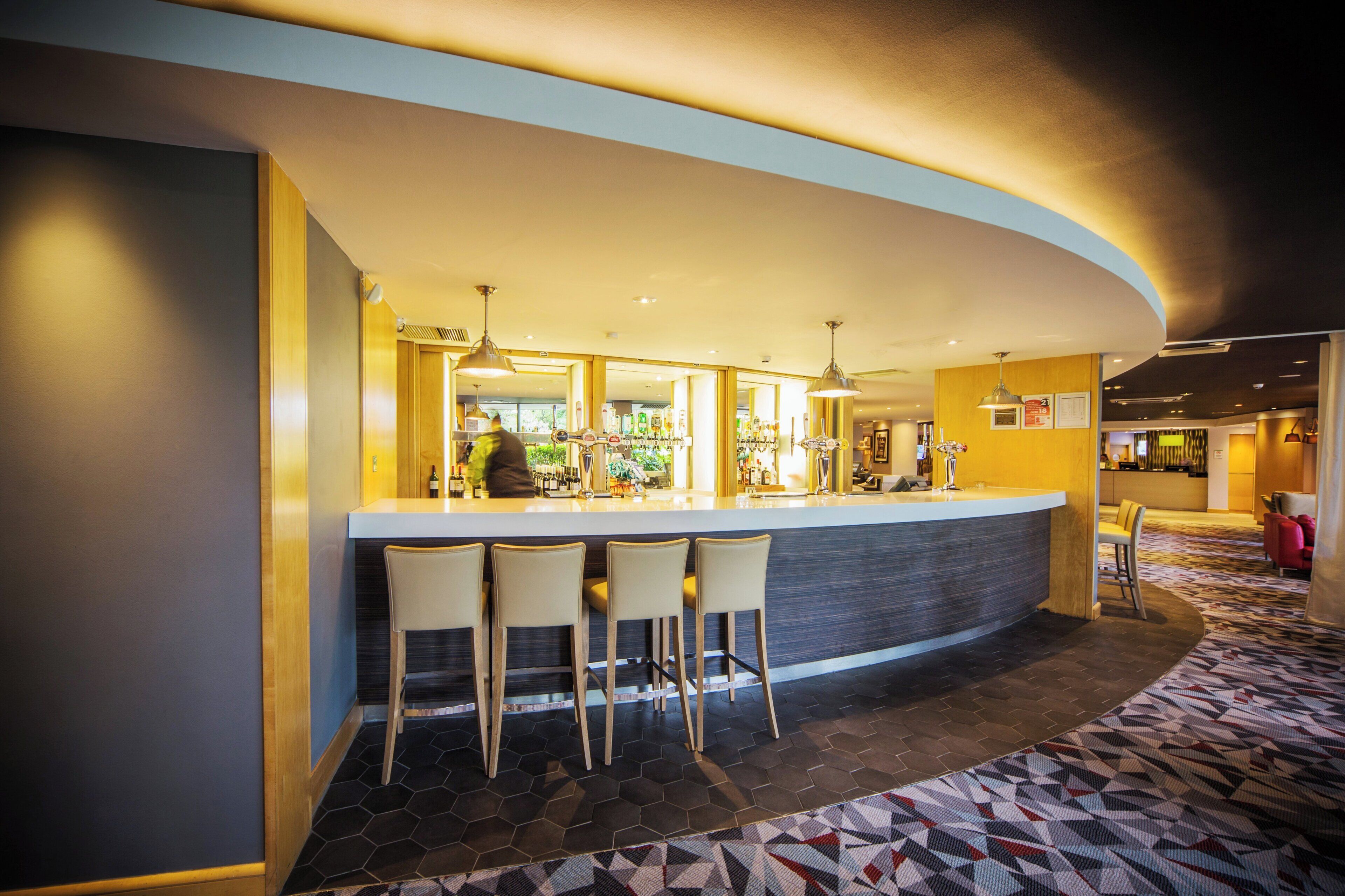 A bar area with a curved counter, three bar stools, and a bartender.