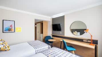 Ein Hotelzimmer mit zwei Betten, einem Schreibtisch, einem Stuhl, einem Fernseher, einem Spiegel und einem kleinen Tisch.