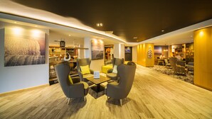 A modern hotel lobby with a wooden floor, seating area with armchairs and a coffee table, a reception desk, and a large painting on the wall. - Holiday Inn Reading South M4 Jct11 by IHG (Reading)