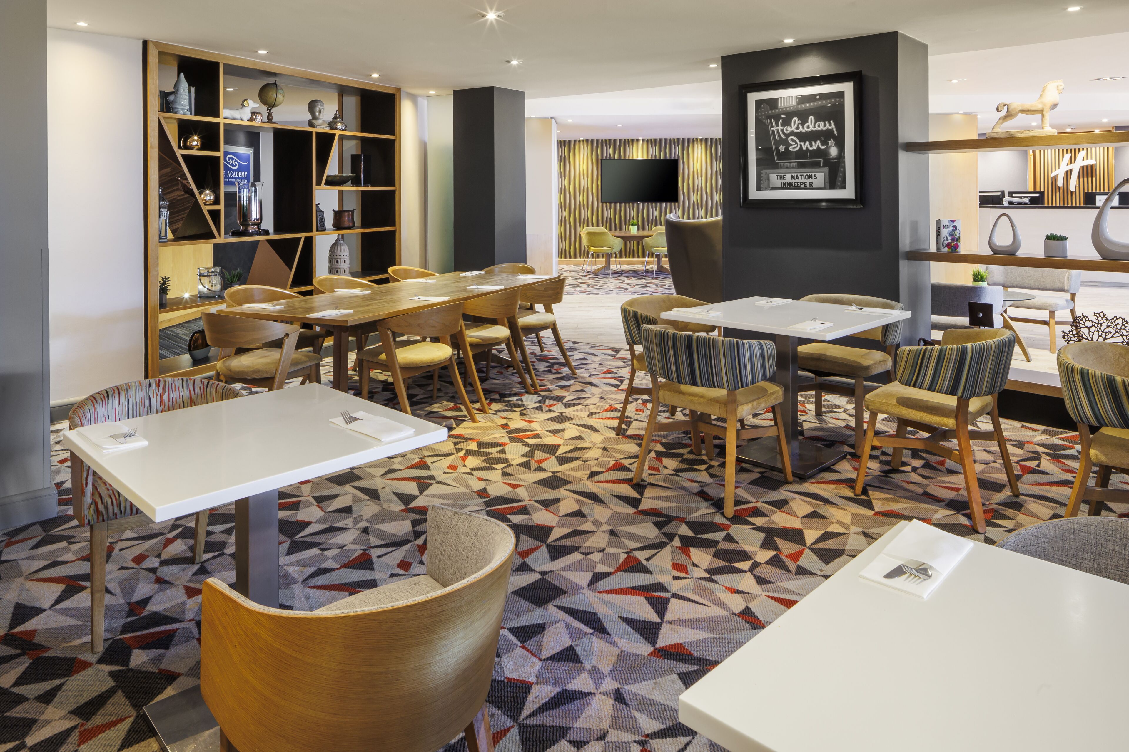 A modern hotel lobby with multiple seating areas, including tables and chairs, and a patterned carpet.