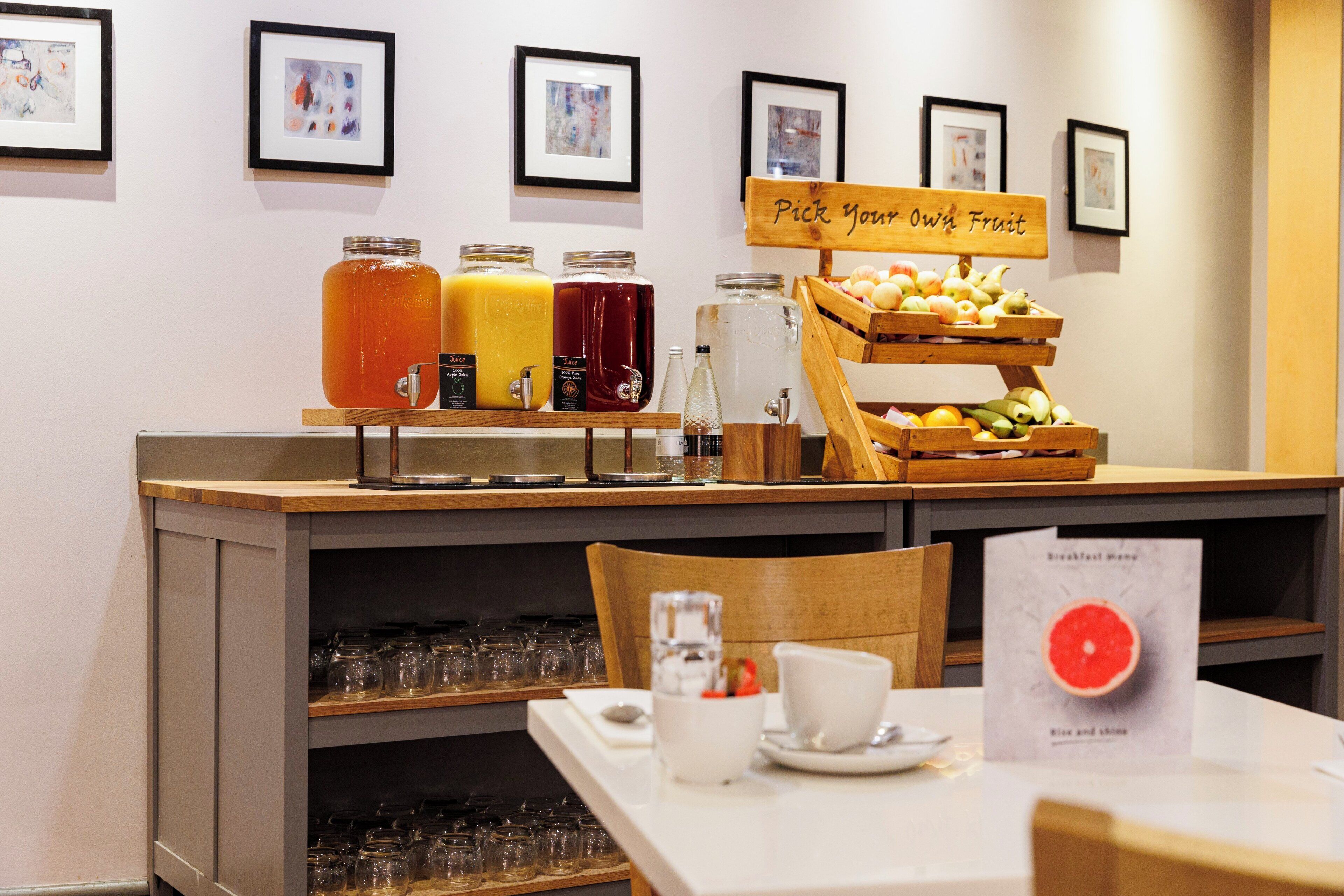 Una barra de desayuno con una exhibición de frutas y dispensadores de bebidas.