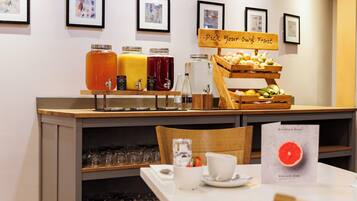 Una barra de desayuno con una exhibición de frutas y dispensadores de bebidas.