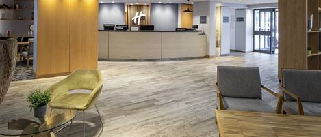 A modern reception area with a wooden reception desk, grey upholstered chairs, and a glass table.