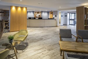 A modern reception area with a wooden reception desk, grey upholstered chairs, and a glass table.