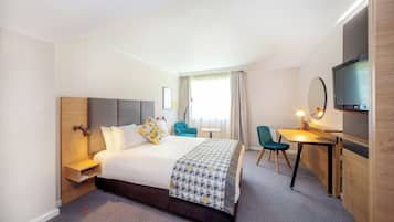 Ein Hotelzimmer mit Bett, Schreibtisch, Stuhl, Fernseher und einem Fenster mit Vorhängen.