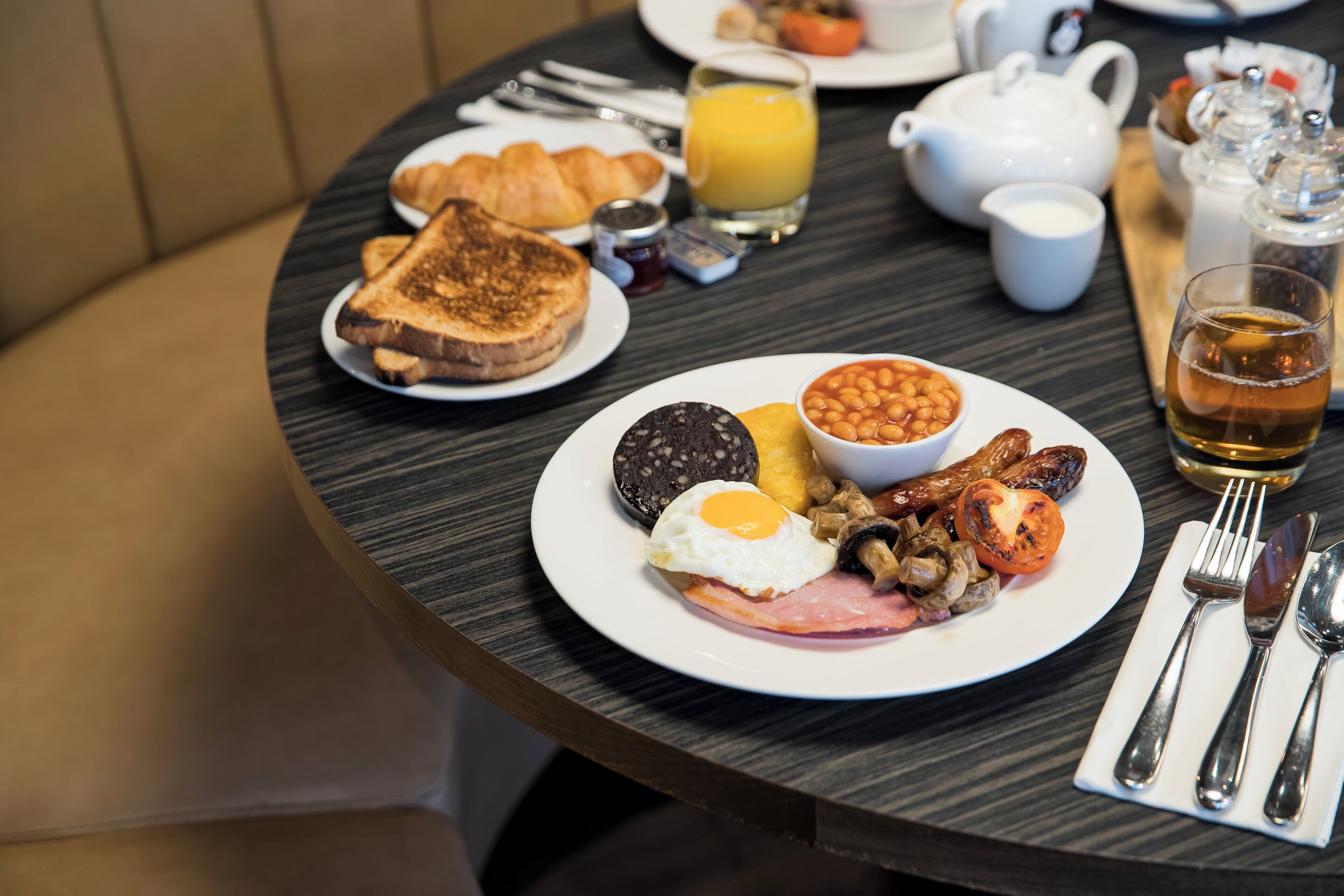 A breakfast setting with toast, eggs, beans, sausages, and a teapot on a round table.