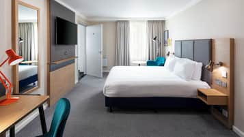 Een hotelkamer met een groot bed, een bureau met stoel, een televisie en een badkamer zichtbaar door een open deur.