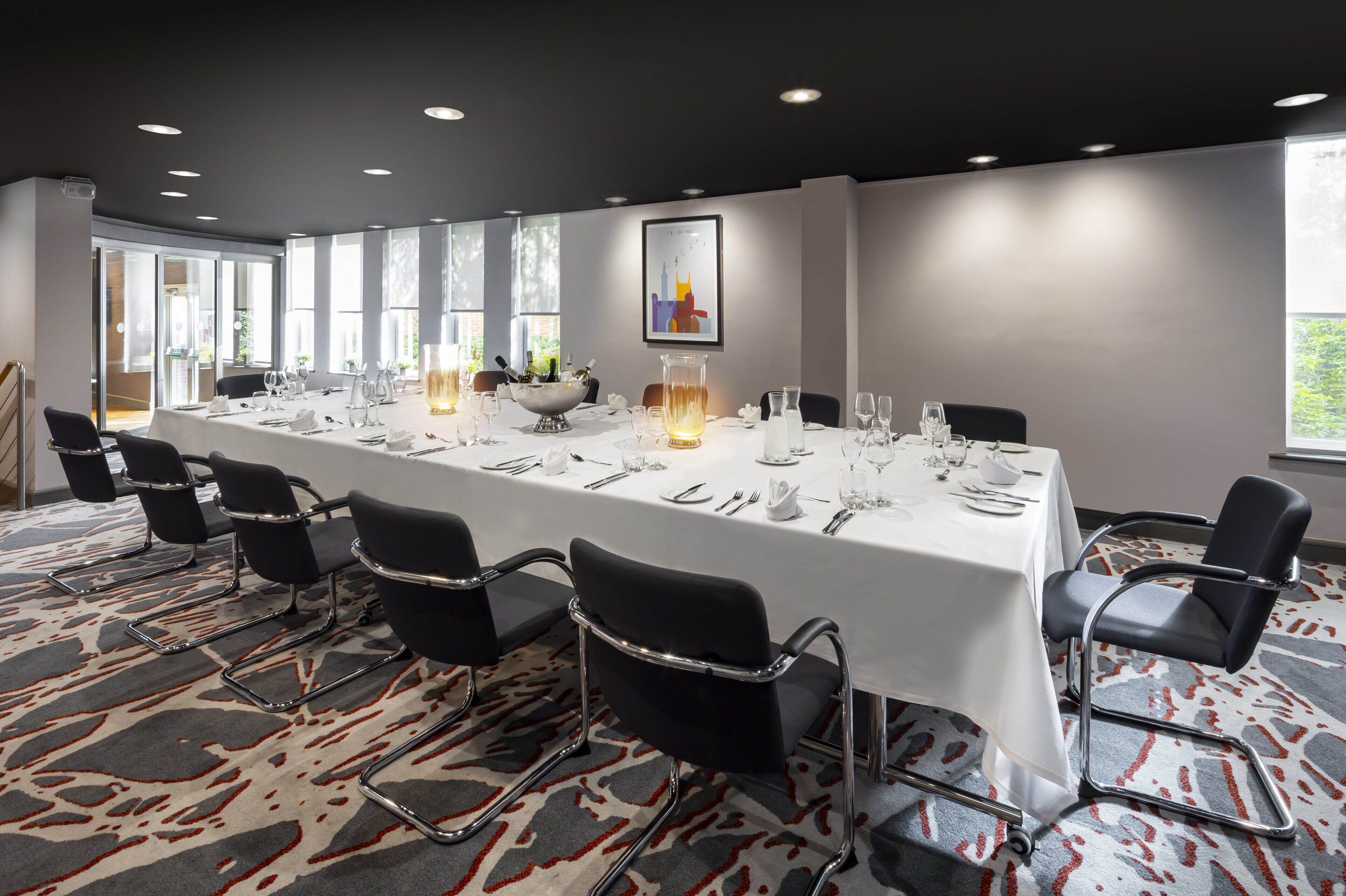 A conference room with a long table set for a meeting, black chairs, and a patterned carpet.