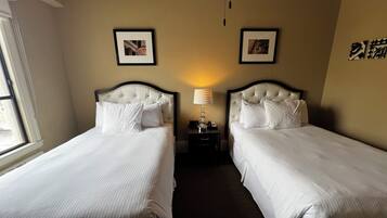 A hotel room with two beds, a nightstand, a lamp, and two framed pictures on the wall.