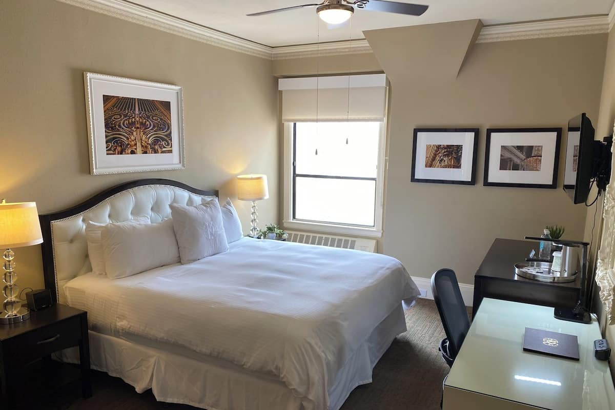 A hotel room with a large bed, bedside lamps, a desk, a chair, and a ceiling fan.