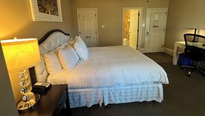 Una habitación de hotel con cama, escritorio, silla, ventilador de techo y lámpara de pared.