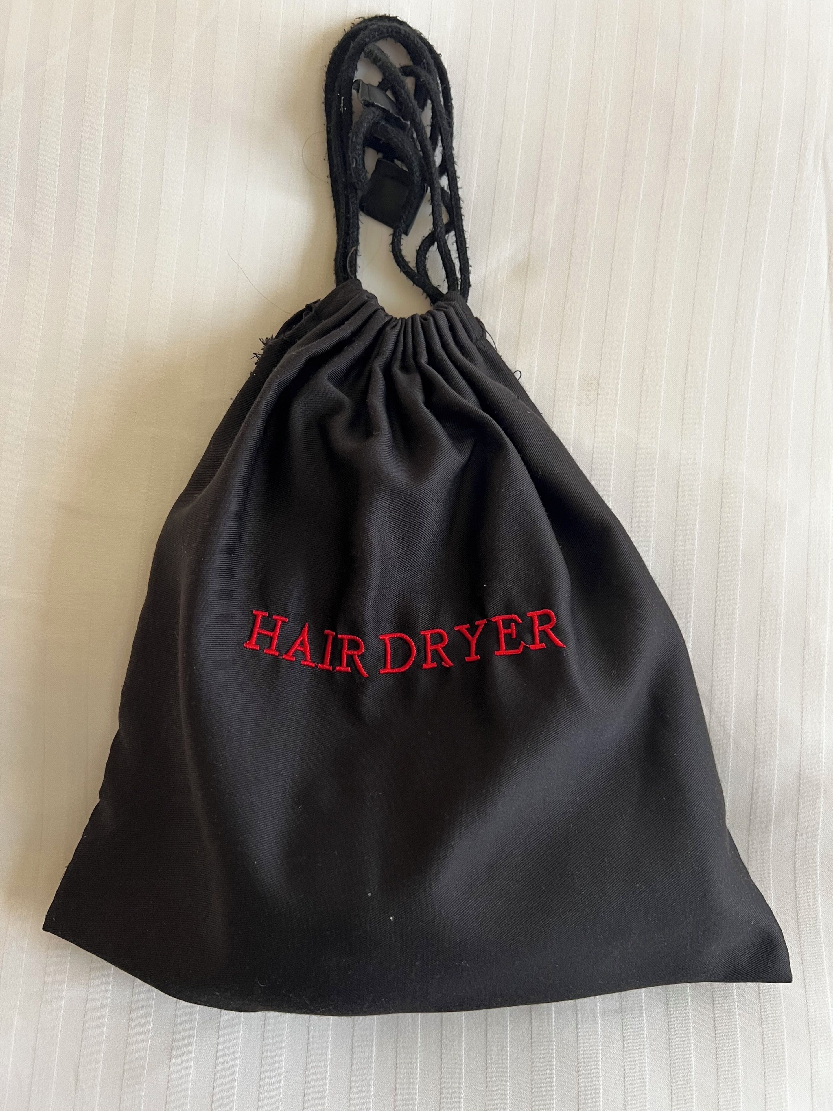 A black drawstring bag with 'HAIR DRYER' embroidered in red.