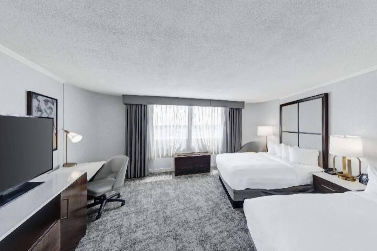 A hotel room with a bed, a desk, a chair, a TV, and a window with curtains.