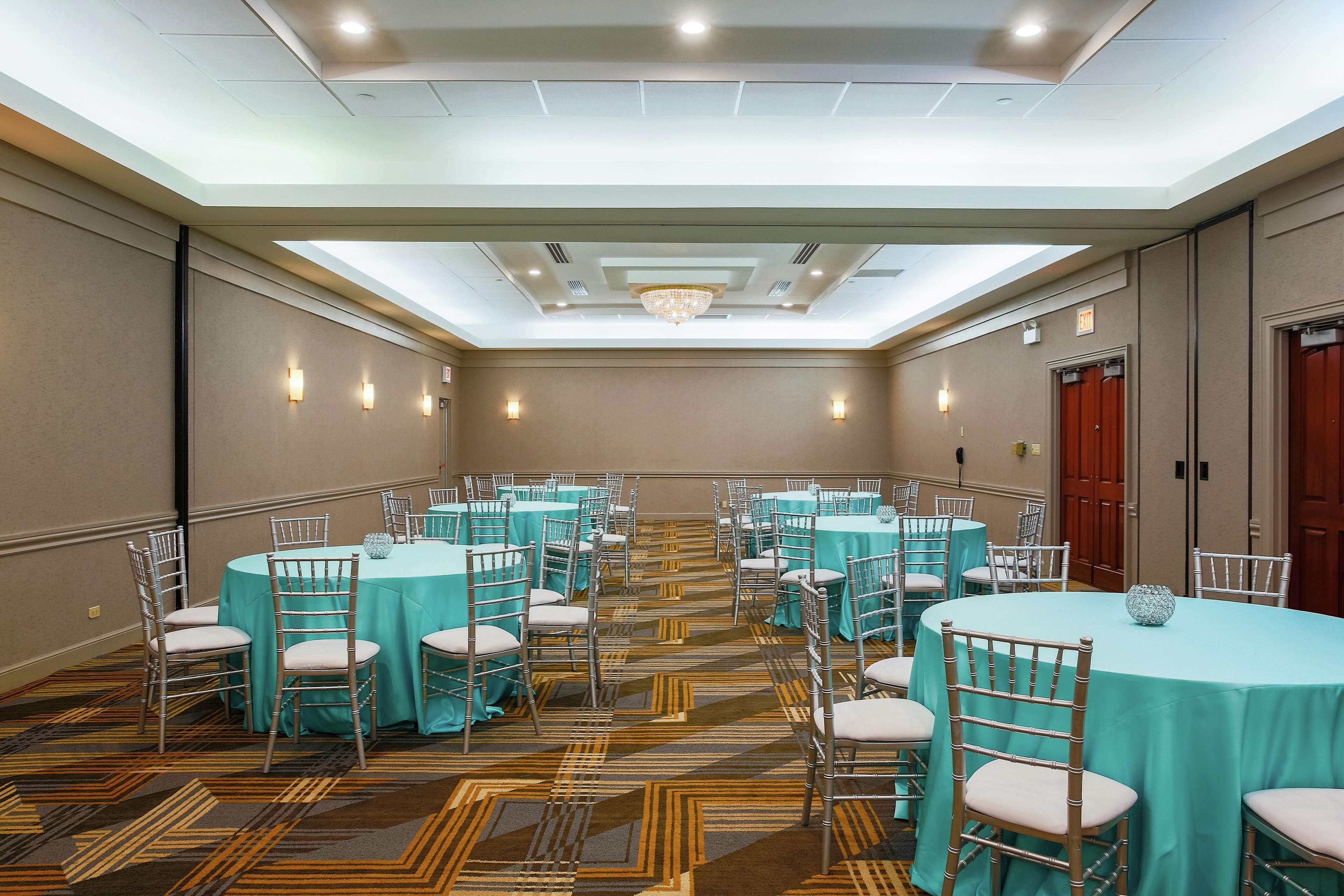 A conference room with multiple round tables, each surrounded by chairs, and a patterned carpet.