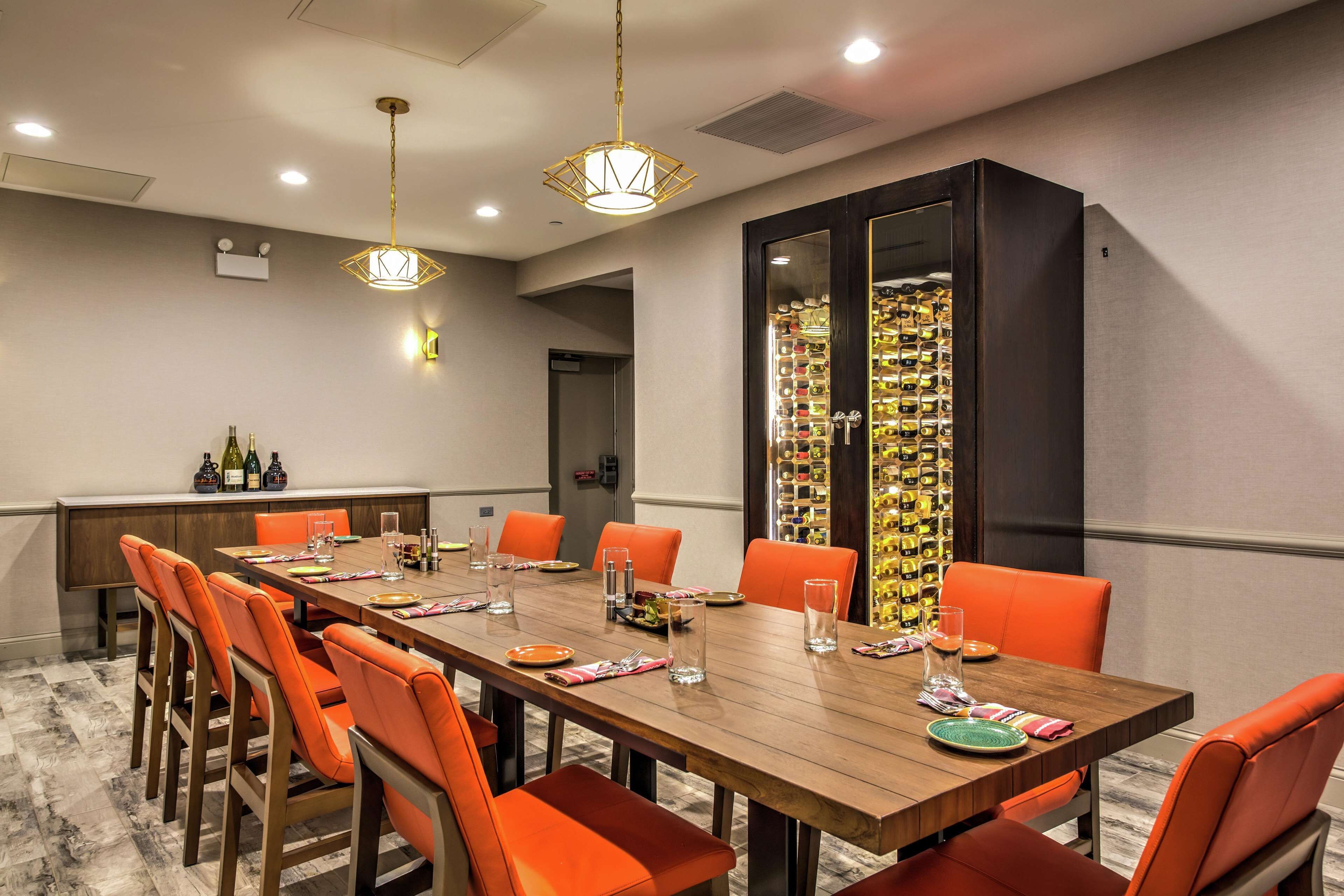 A conference room with a long wooden table, orange chairs, and a wine rack.