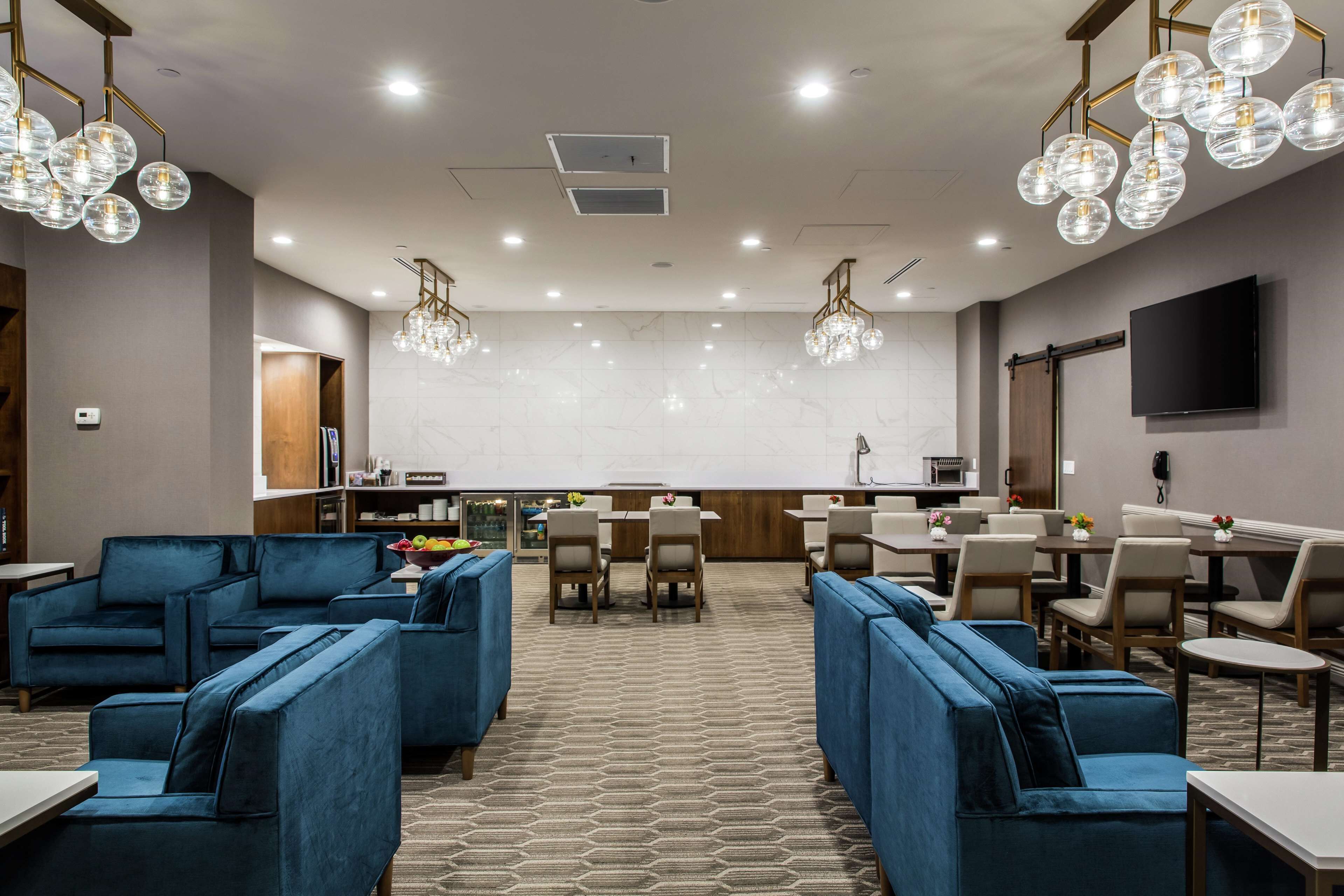 Un moderno vestíbulo de hotel con sofás azules, una zona de bar y un televisor de pantalla plana.