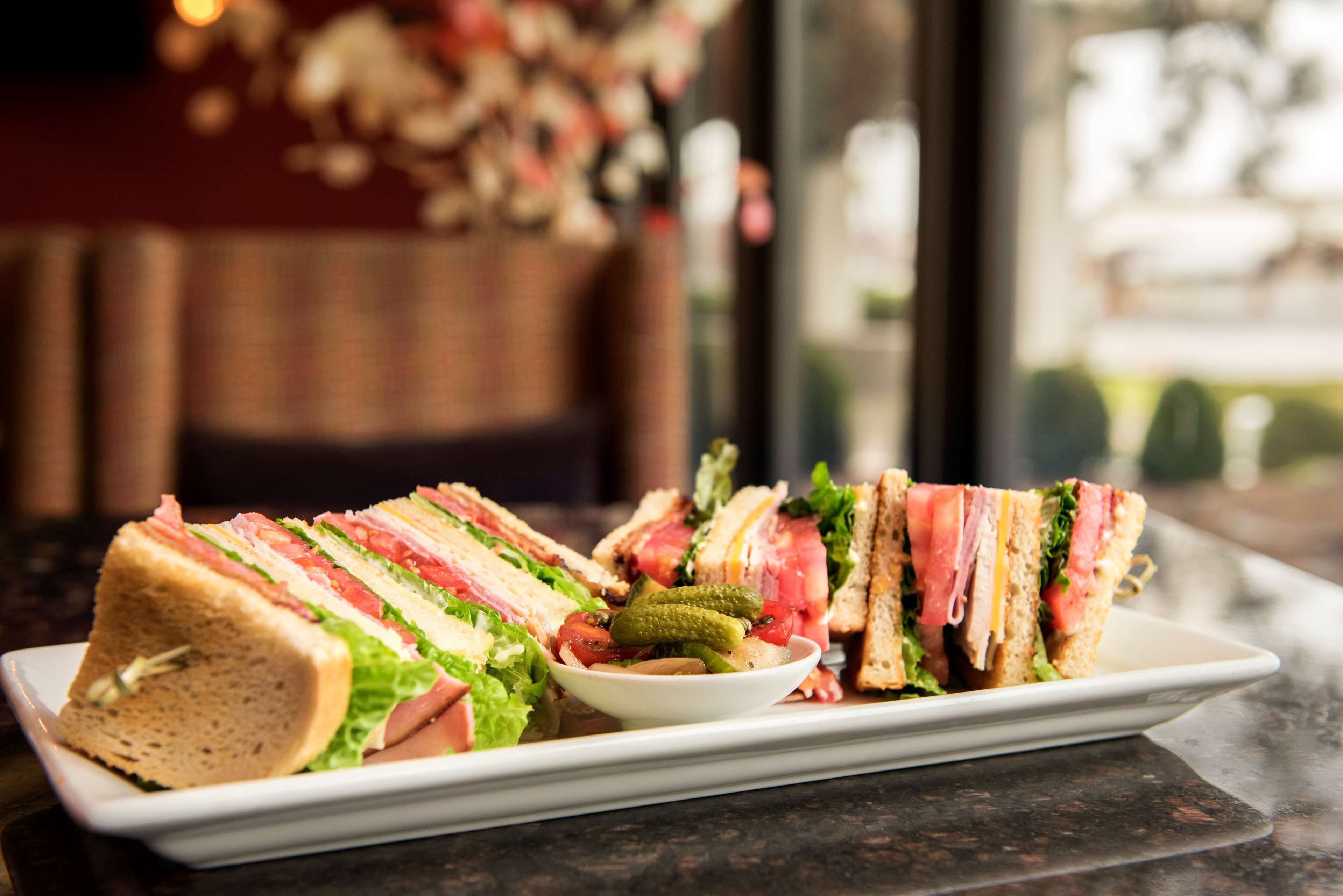 A plate with several sandwiches and a small bowl of pickles.