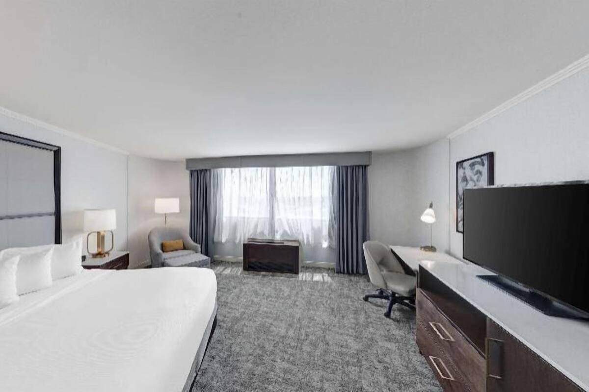 A hotel room with a large bed, a desk, a chair, a TV, and a window with curtains.