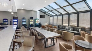 Een ruime binnenzone met een lange tafel, meerdere stoelen, een bank en verschillende speelautomaten.