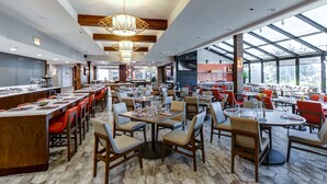 Een ruim restaurant met hoge plafonds, grote ramen en diverse zitmogelijkheden, zoals tafels en stoelen.