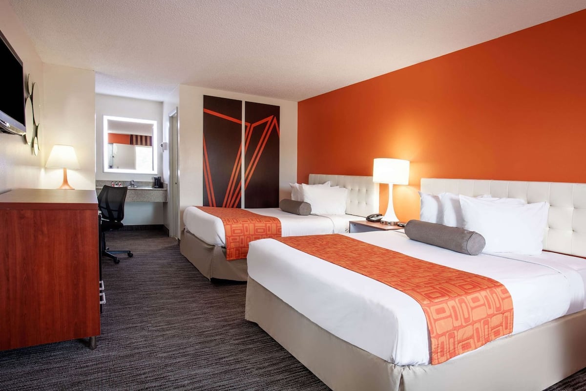 A hotel room with two beds, a desk, a chair, a TV, and a bathroom visible through an open door.