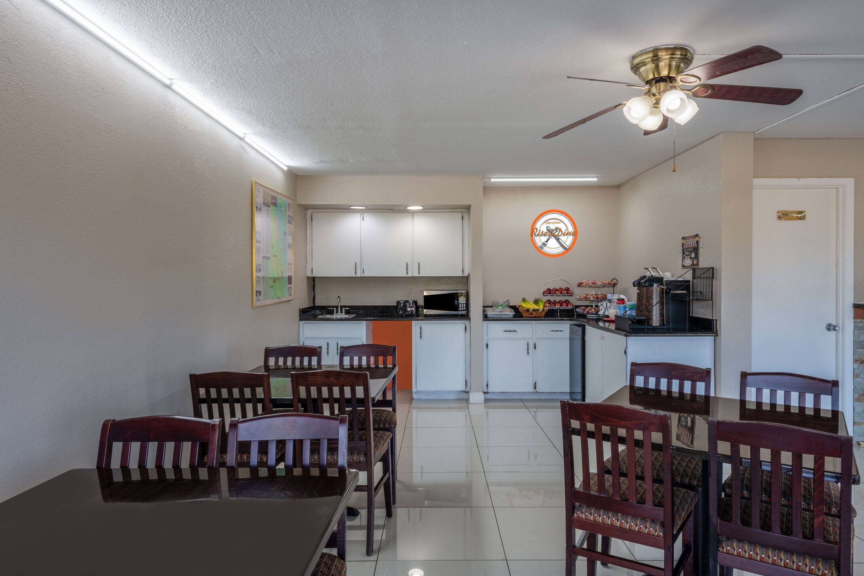 A dining area with a table and chairs, a kitchen in the background, and a ceiling fan.