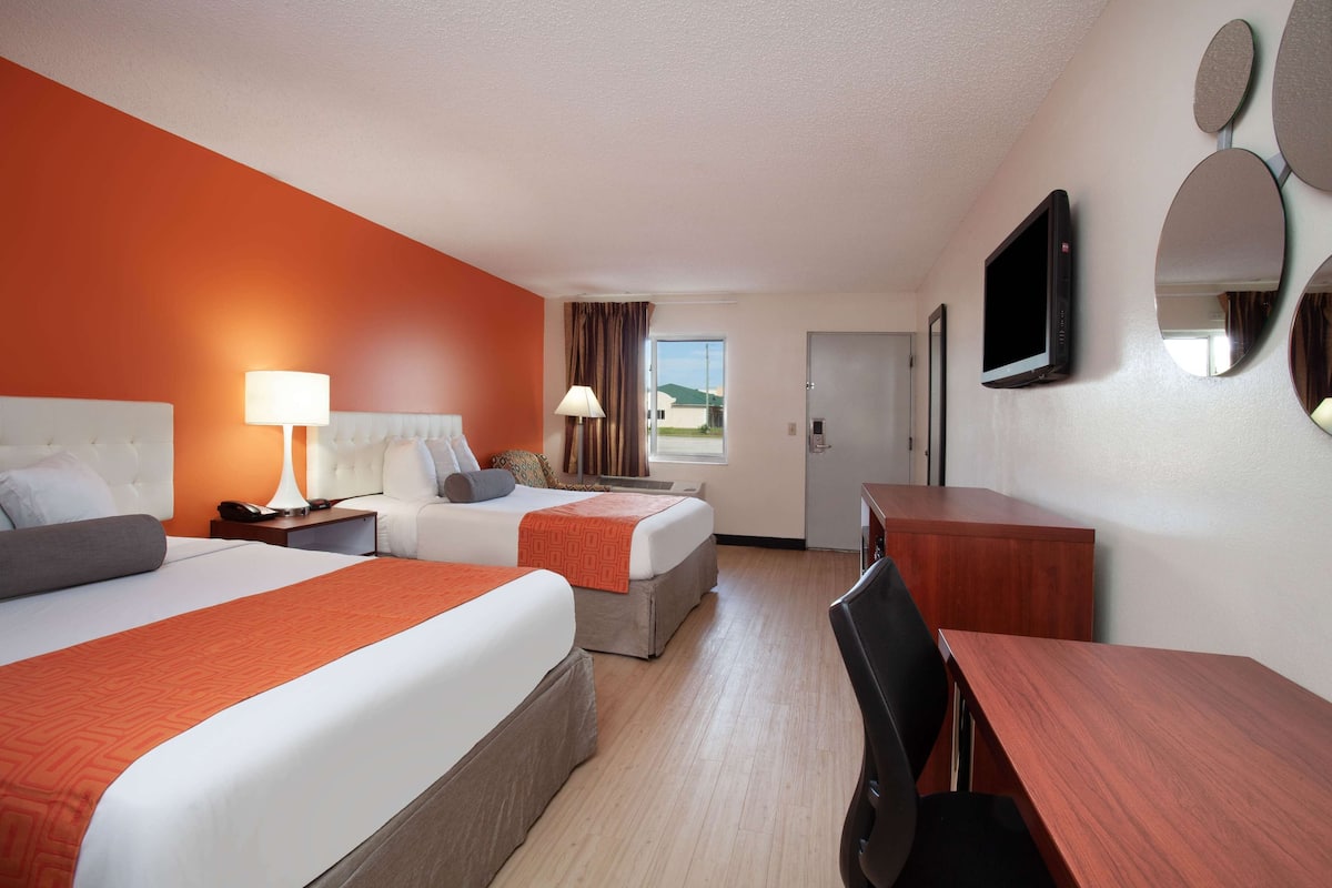 A hotel room with two beds, a desk, and a TV.