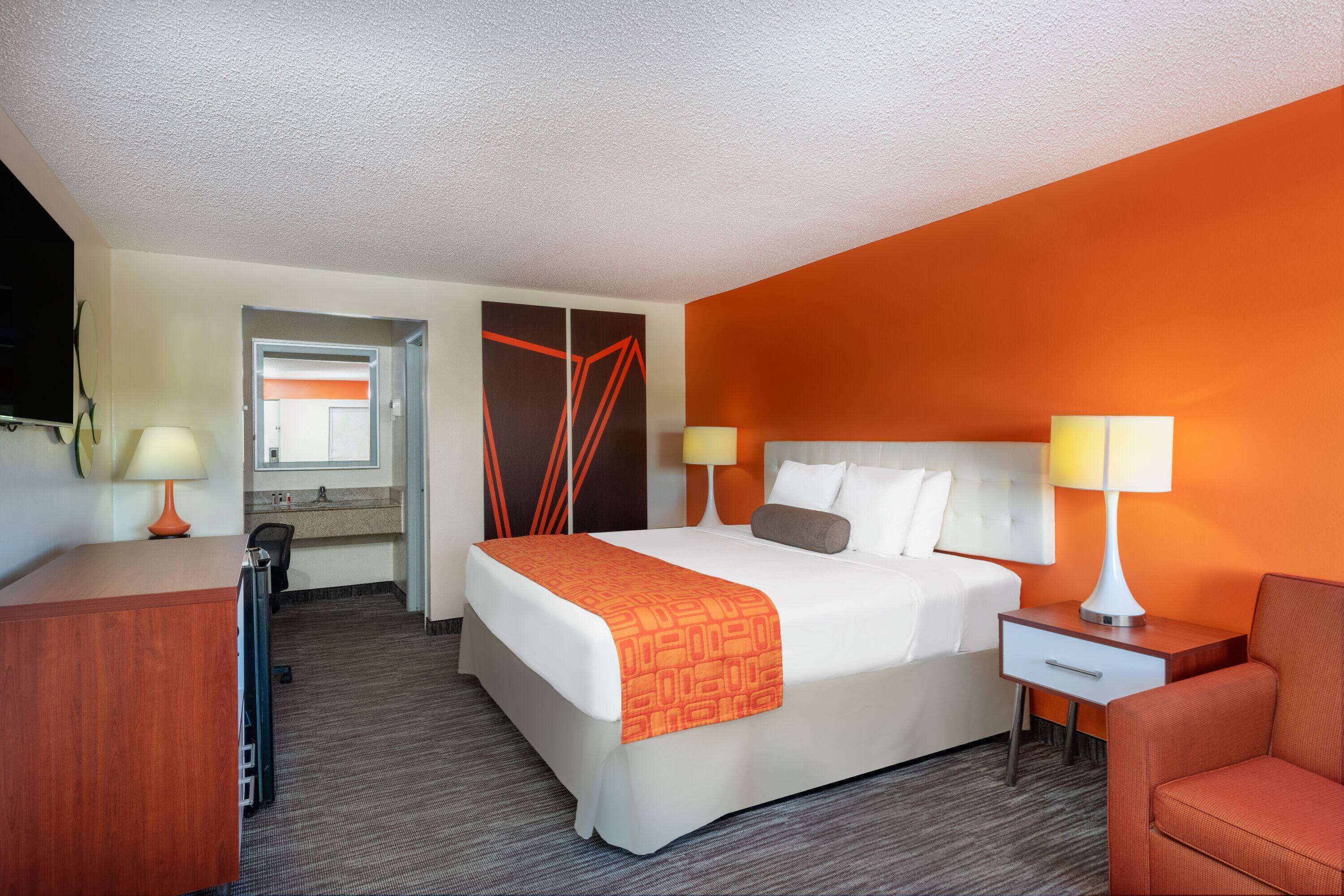 A hotel room with a bed, bedside tables, a desk, and a chair.